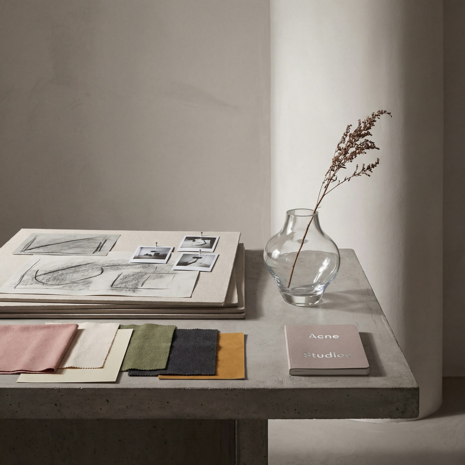 Fabric swatches, charcoal sketches, reference photos, and a glass vase arranged on a design table